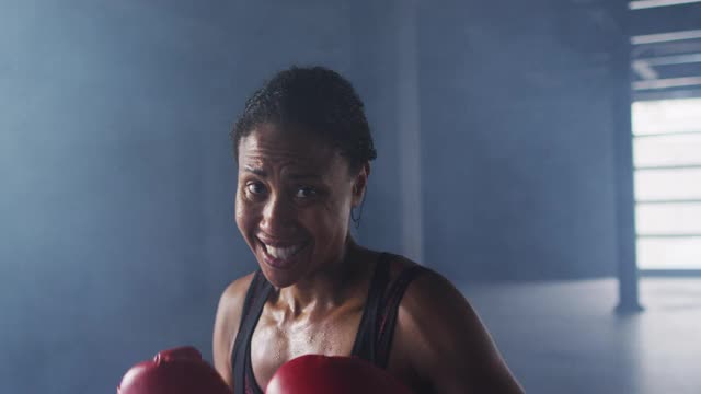 非洲裔美国妇女戴着拳击手套在空房间里训练投掷拳头视频素材