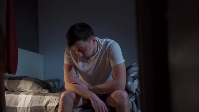 患有严重头痛的人晚上在床上吃药。抑郁的男性坐在床上，服用安眠药或过夜的药物。患有失眠症。担心卧室噩梦的人视频下载