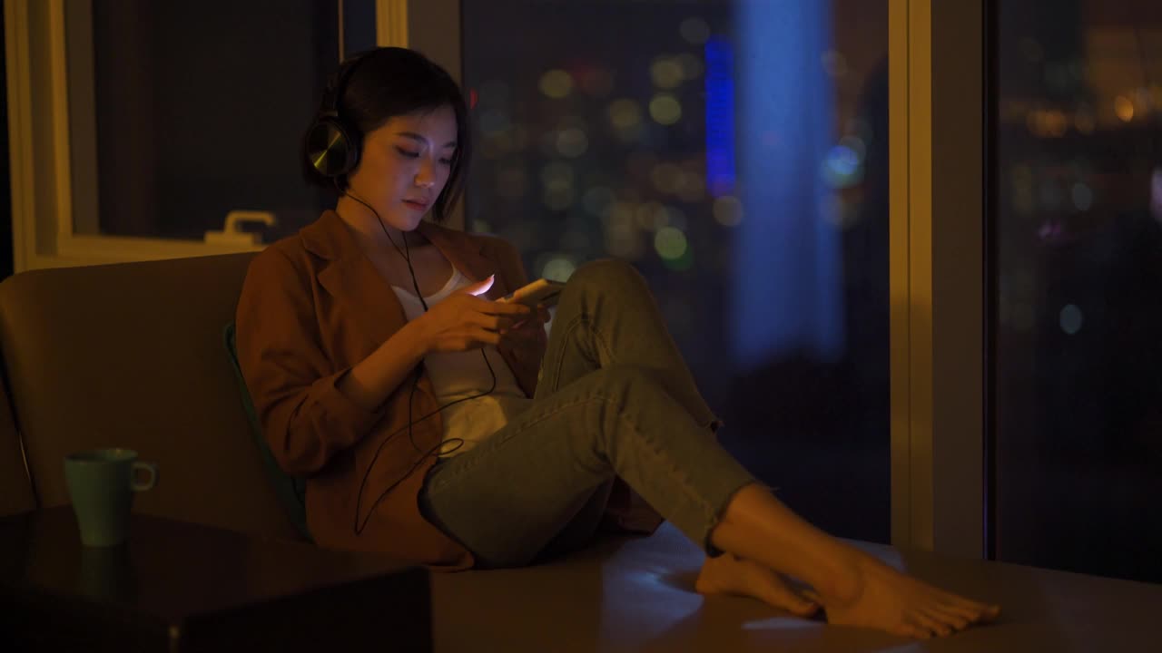 年轻的亚洲华人女子在晚上的客厅里用手机上网视频素材