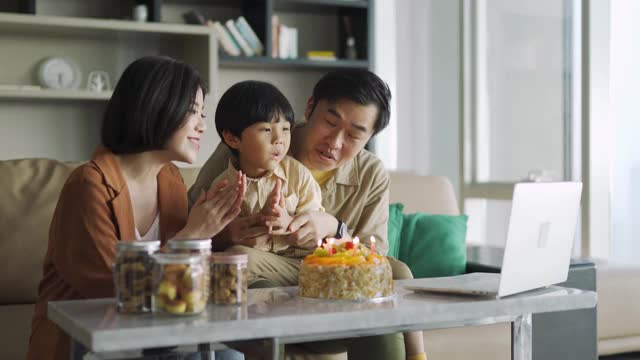 可爱的亚洲华人孩子与他的父母和祖父母在网上视频聊天庆祝他的生日蛋糕视频素材