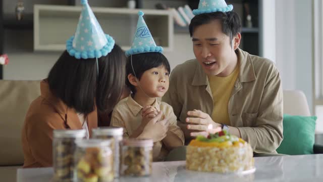 可爱的亚洲华人孩子和他们的父母吹生日蜡烛视频素材