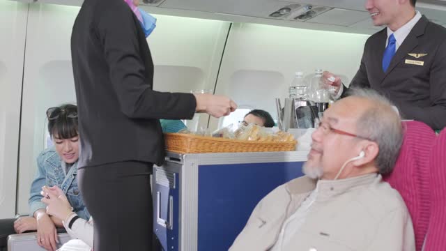 在飞机的经济舱上，空姐或乘务员为高级乘客提供软饮料。戴耳机，穿夹克。感到口渴，放松一下。航空服务与职业理念视频素材