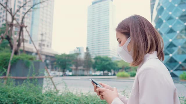 在空荡荡的城市街道上，女商人戴着医用口罩走路或打手机。视频素材