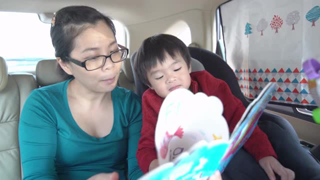 亚洲母亲在开车旅行时和男婴读了一本书。视频素材