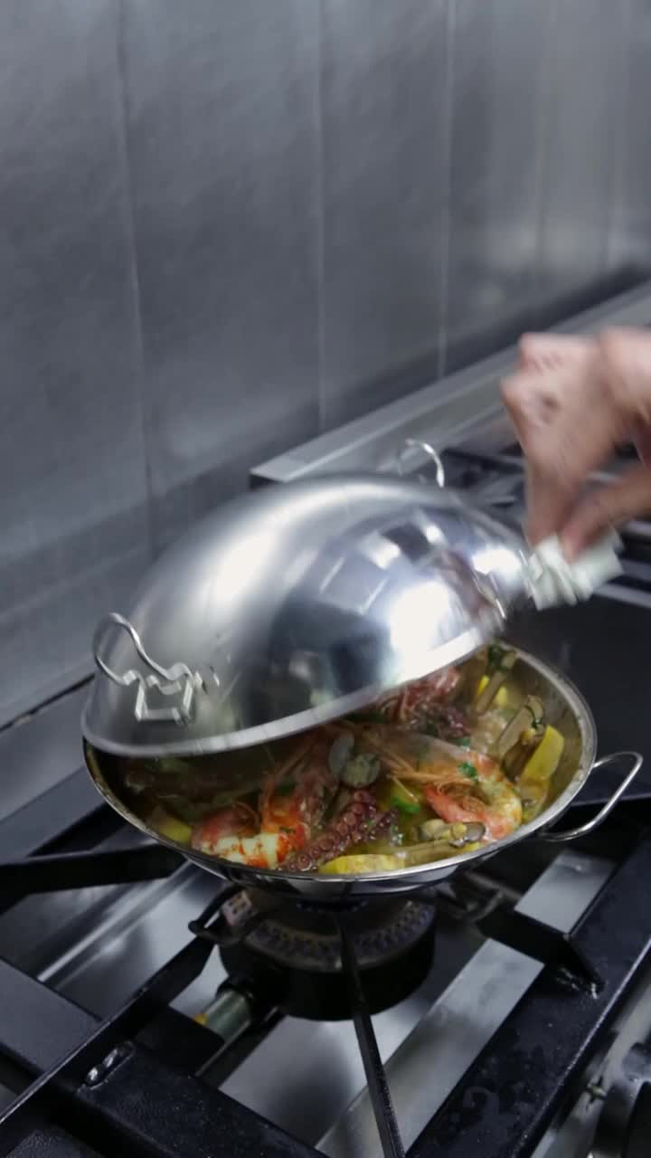 厨师在煤气炉上取下烹饪海鲜和蔬菜的餐盘盖。垂直视频。特写镜头。视频下载