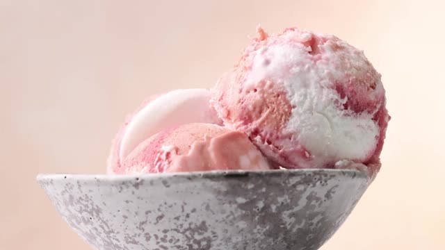 近距离的三个粉色水果冰淇淋球在一个碗旋转米色的背景视频下载
