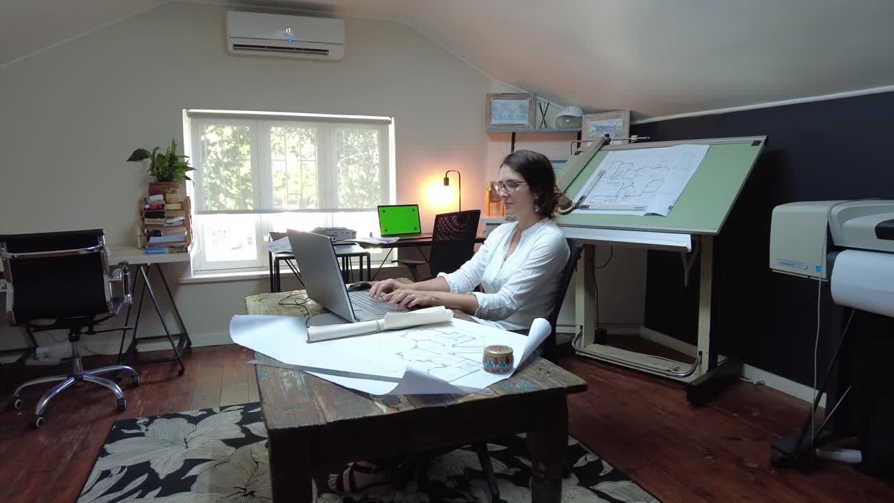 Dolly在侧视图年轻女建筑师在办公室的笔记本电脑上工作，建筑计划开放视频下载