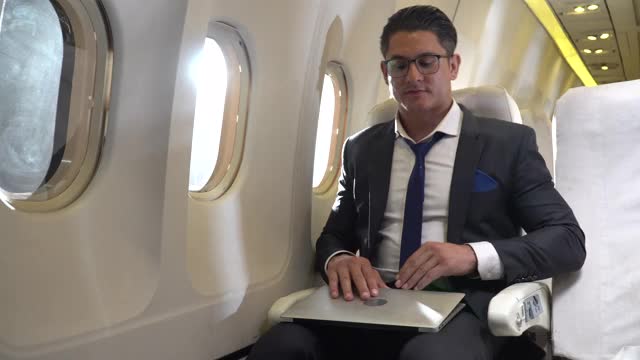商人坐在飞机上用笔记本电脑工作，有阳光照射视频下载