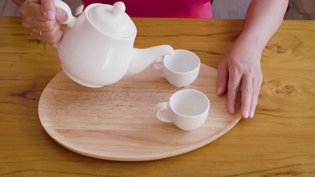 女子从茶壶倒进木桌上的茶杯中，茶道概念视频素材