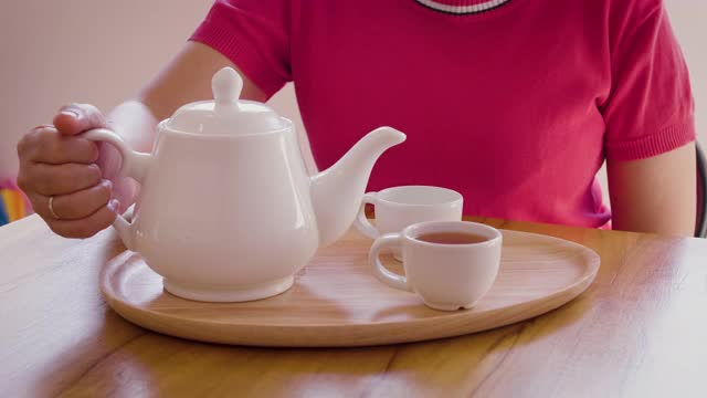 女子从茶壶倒进木桌上的茶杯中，茶道概念视频下载