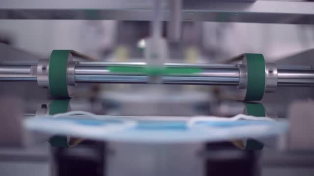 在A工厂的口罩生产线上，特写机器人手臂将防护口罩推到跑步带上视频素材