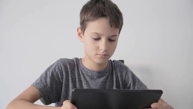 专注的孩子使用数字平板技术设备。男孩抱着平板电脑看视频，在线学习，上网，在家里玩游戏。视频素材