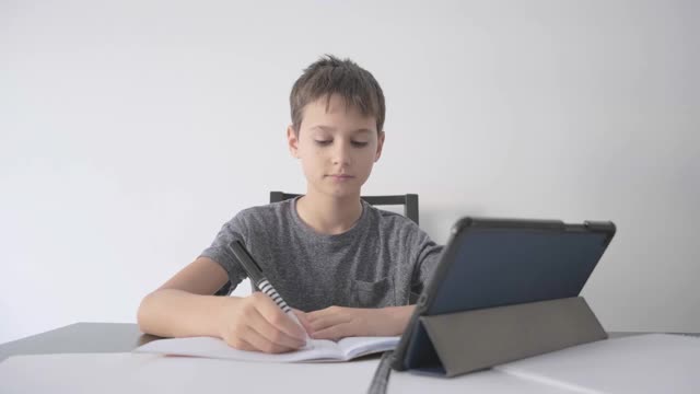 在线学习，远程课程，在家教育，儿童科技。男孩用教科书做家庭作业，在家里用数码平板电脑。视频素材