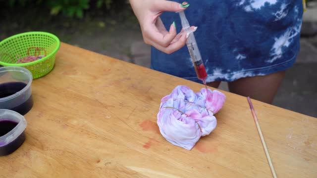 年轻的亚洲妇女练习在白色t恤上处理扎染织物在家里，家庭教育的概念视频下载