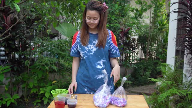年轻的亚洲妇女练习在白色t恤上处理扎染织物在家里，家庭教育的概念，成功的手势视频下载