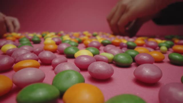 两个人在粉红色的背景下把绿色的软糖和其他软糖分开视频下载