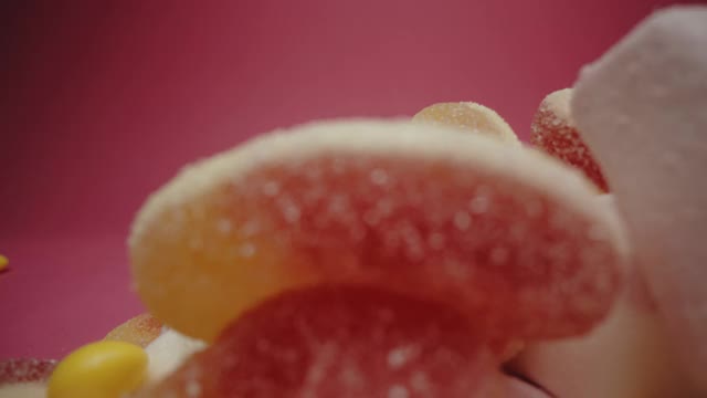 粉红色背景上有棉花糖、软糖和五颜六色的酸糖视频下载