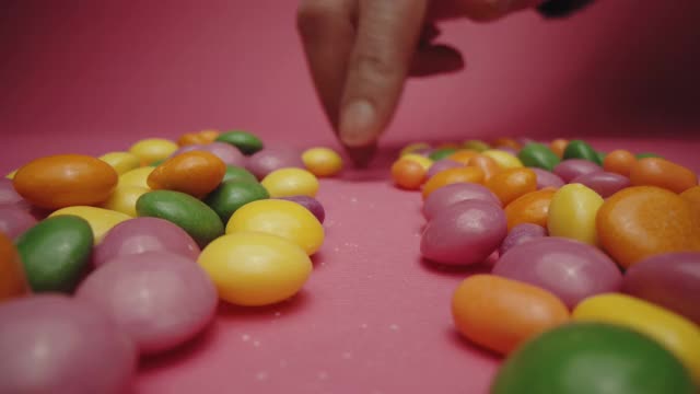 女性手指走过一堆糖果在粉红色的背景视频下载