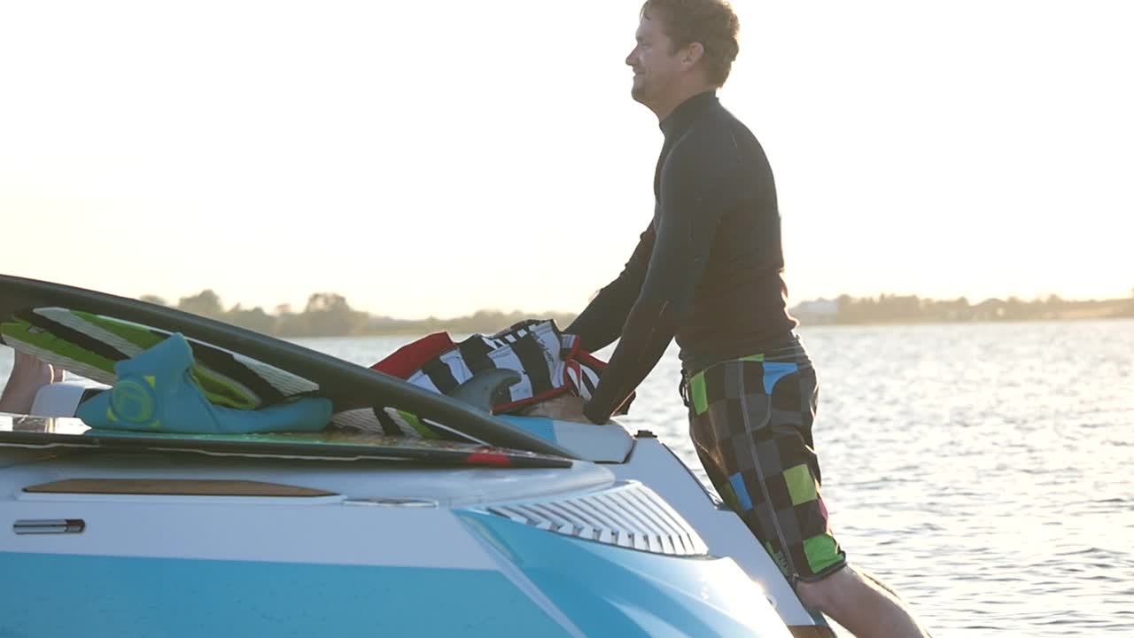 一个穿着救生衣的男人准备在湖上的小船后面冲浪。视频下载