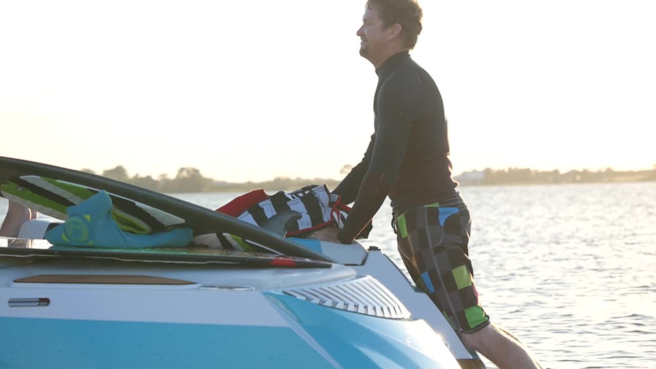 一名男子穿上救生衣准备在湖上的一艘小船后面进行尾流冲浪。——慢动作视频下载