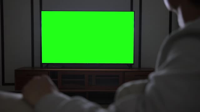 男人在看绿色屏幕的电视视频素材