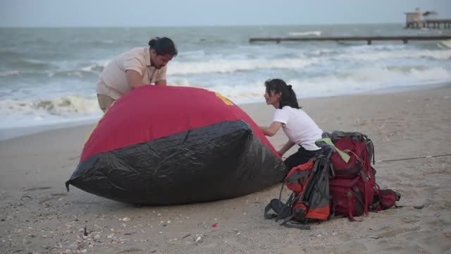 徒步旅行和露营概念。一对亚洲游客夫妇在海边帮忙搭帐篷。视频下载