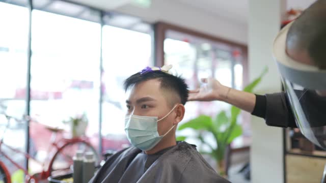 穿着防护服的亚洲华人发型师在发廊为他的顾客理发视频下载