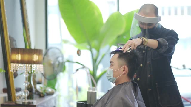 穿着防护服的亚洲华人发型师在发廊为他的顾客理发视频素材