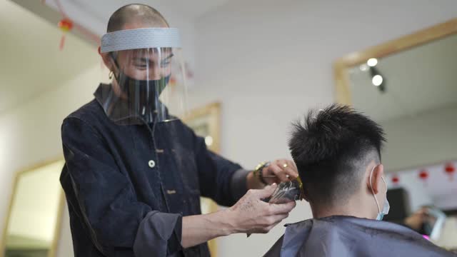 穿着防护服的亚洲华人发型师在发廊为他的顾客理发视频素材