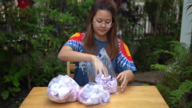 年轻的亚洲妇女练习在白色t恤上处理扎染织物在家里，家庭教育的概念，成功的手势视频下载
