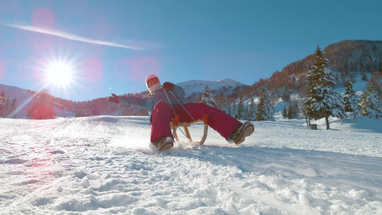 低角度:在一个阳光明媚的日子里，快乐的年轻女子骑着雪橇从雪山上滑下来。视频素材