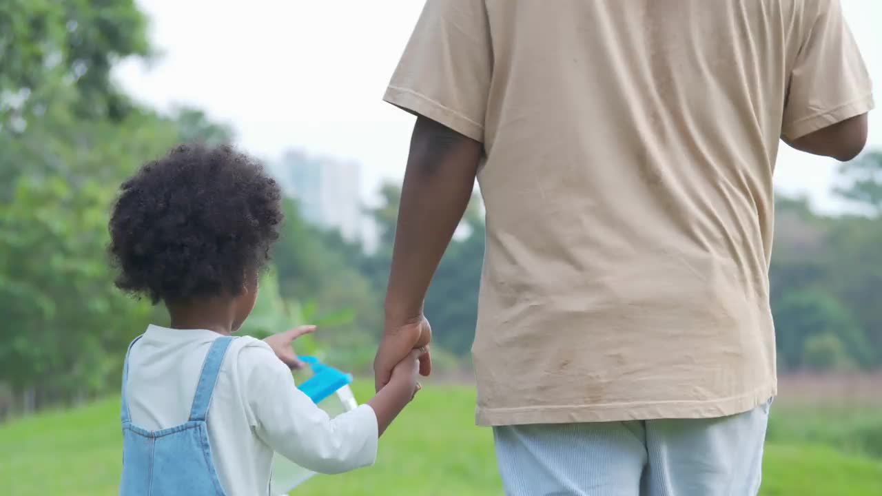 后视图非洲父亲和4岁的儿子手拉手在公园散步，同时一起教授和学习可持续发展的自然资源。援助之手的概念。视频素材