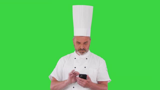 成熟的厨师穿着白色制服在绿屏上用手机发短信，色度钥匙视频下载