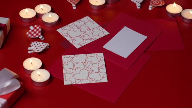 女人的手在情人节卡片上画一个心形标志。俯视图红色桌子与燃烧的蜡烛，装饰心和礼品盒。情人节的概念。浪漫的心情。关闭了。慢动作视频下载