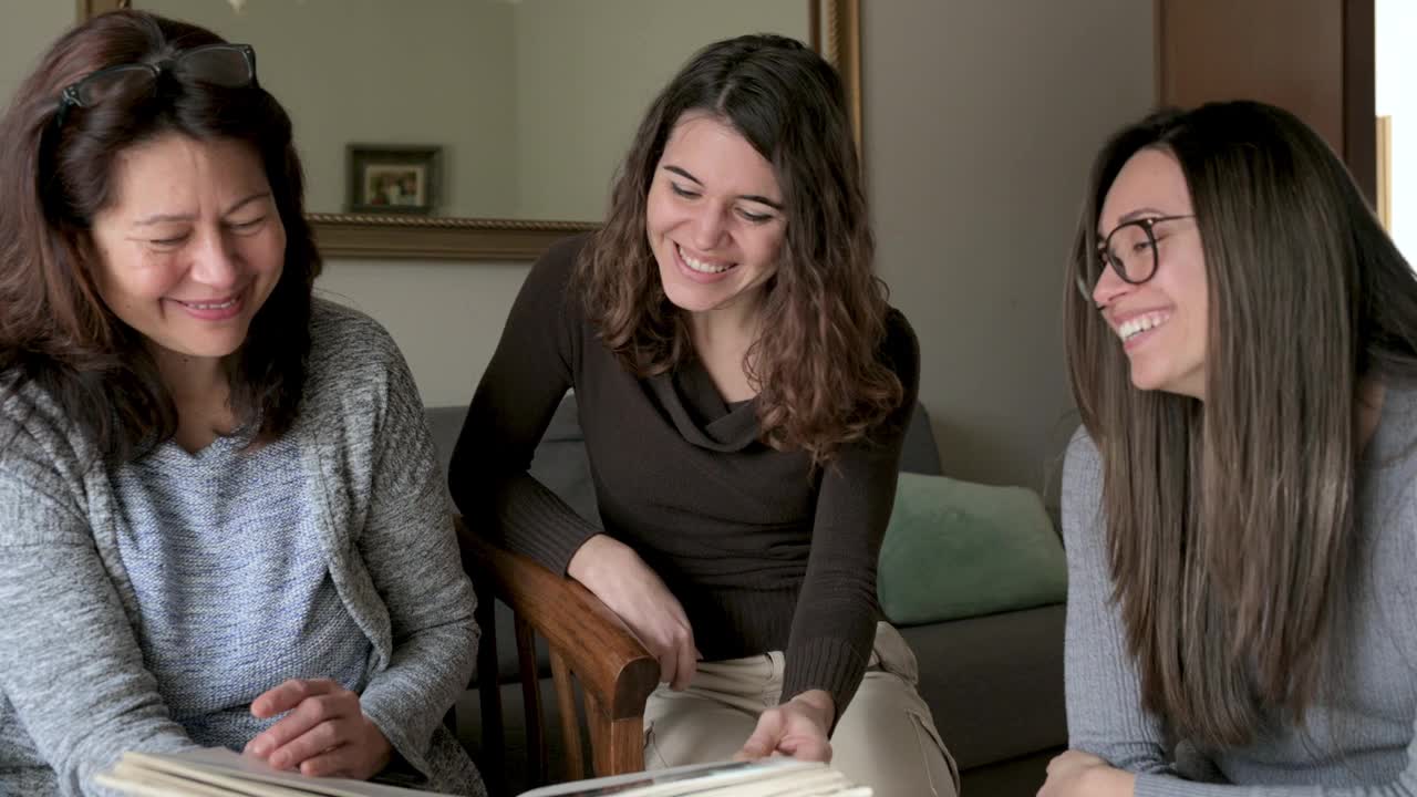 积极的女性坐在沙发上看相册。母亲，女儿，姐妹脸上都洋溢着积极的快乐。记忆,家庭的概念。视频素材