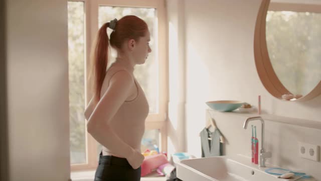 年轻女子早上站在浴室镜子前视频下载