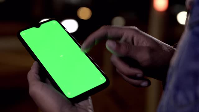 一名男子晚上在户外用绿屏手机滚动屏幕视频下载