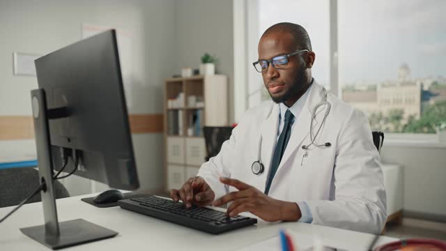 穿着白大褂的富有经验的非裔美国男医生在办公室用个人电脑工作。医疗保健专业人员处理测试结果，病人治疗计划。视频素材