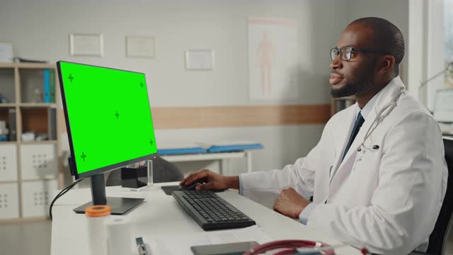 身穿白大褂的资深非裔美国男医生在绿屏模拟显示器电脑上工作。医疗保健专业人员处理测试结果和病人治疗。视频素材