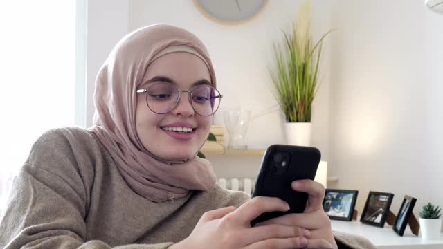 一名中东妇女坐在沙发上，悠闲地玩着智能手机视频素材