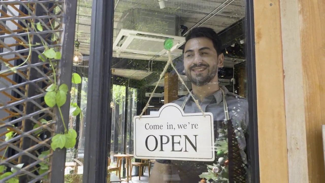 咖啡店的老板把关门的招牌改为开门，欢迎新顾客。视频素材