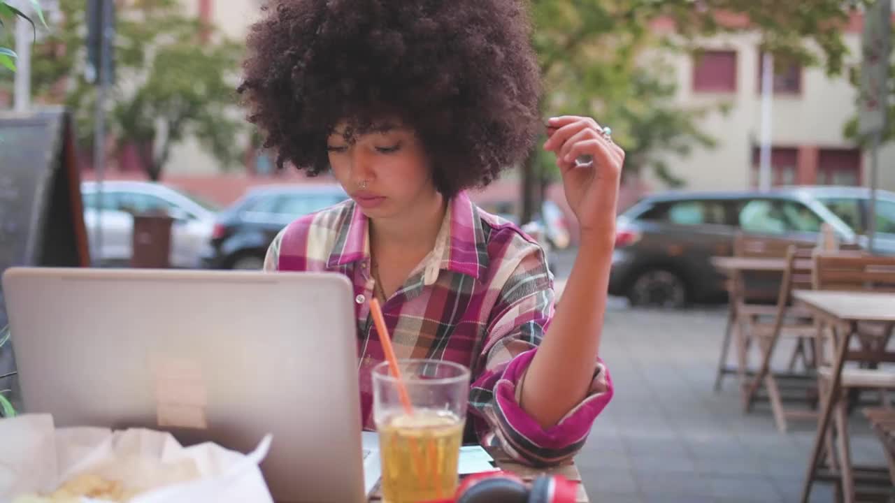 一名年轻女子在路边咖啡馆使用笔记本电脑和智能手机视频下载
