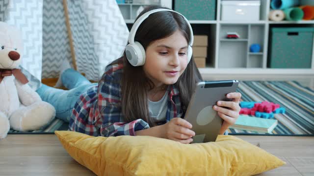 开朗的女孩戴着耳机听音乐，在家里用平板电脑视频素材