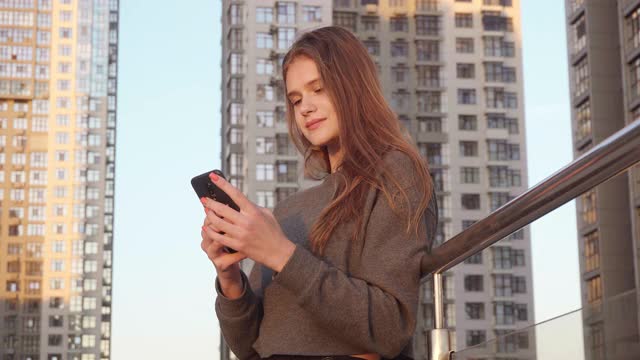 在建筑外部背景中微笑的年轻女子在社交网络中使用短信视频素材