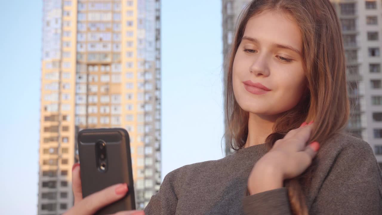 微笑的年轻快乐的女人使用智能手机在社交网络特写，在建筑外部背景视频素材