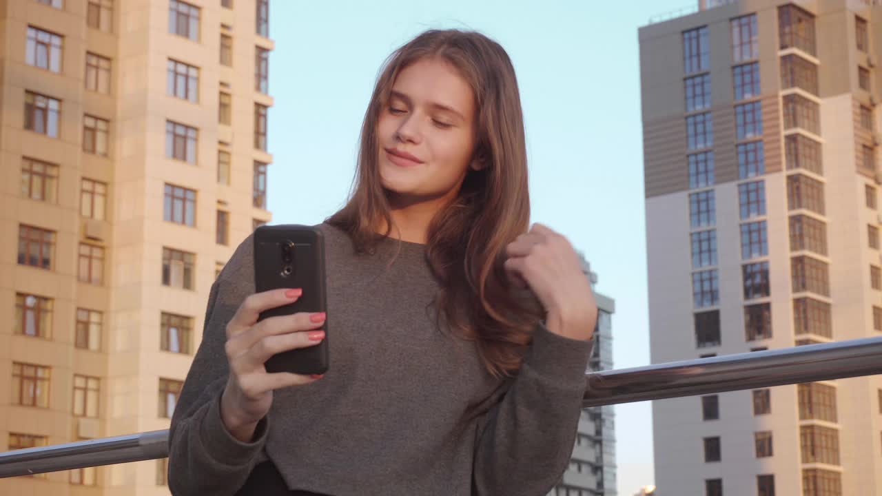 微笑的年轻女子使用视频信息社交网络在建筑外部背景视频素材