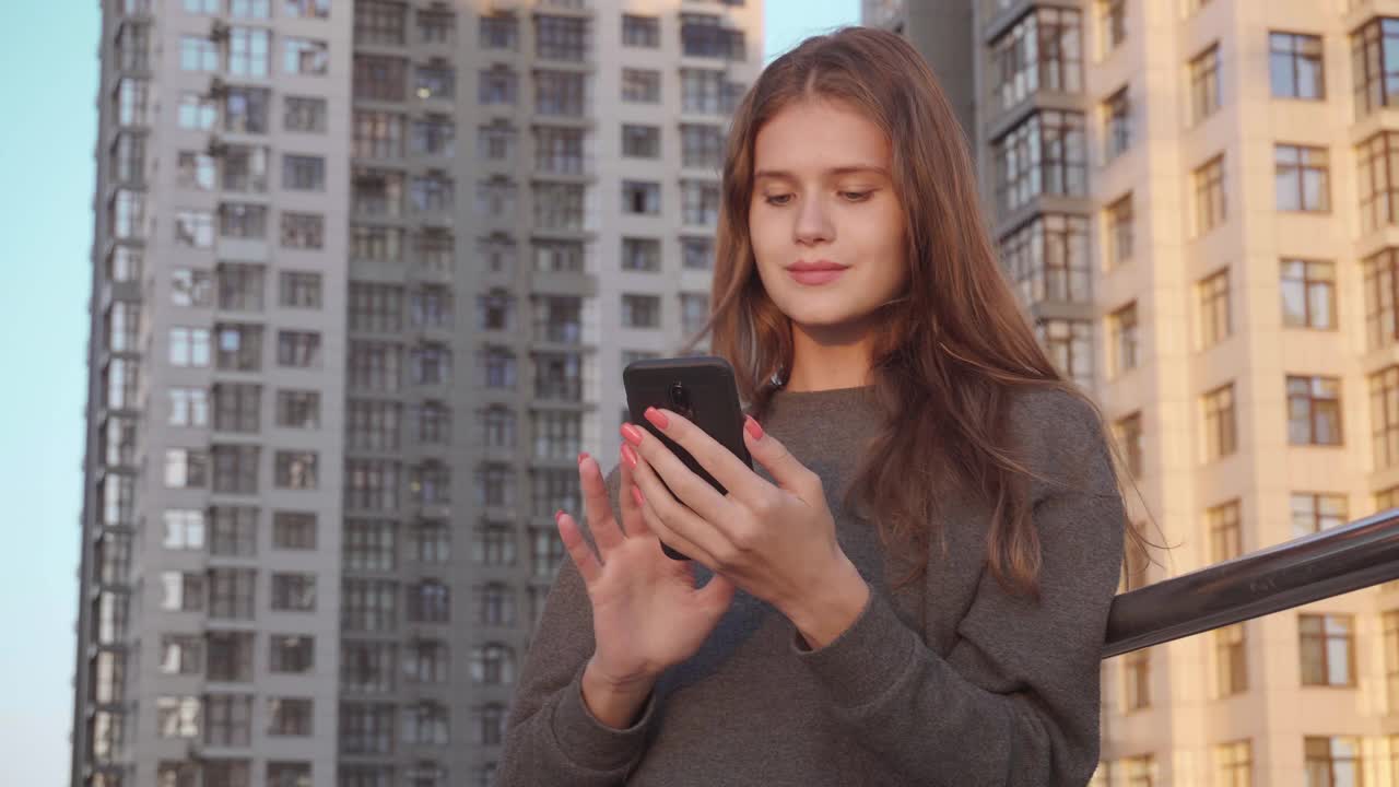 年轻女子在建筑物外部背景下使用社交网络的短信视频素材