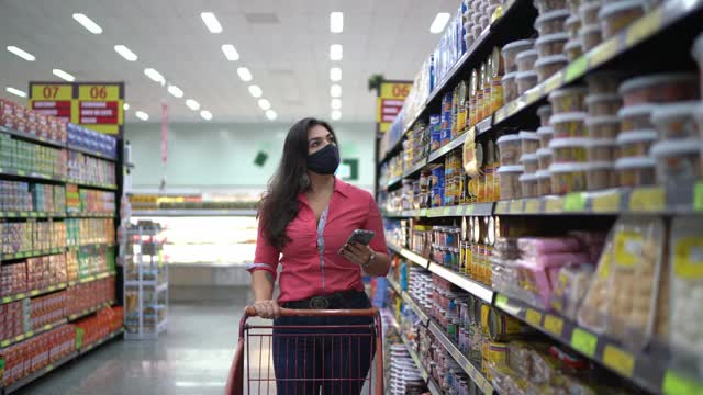 年轻女子戴着口罩在超市过道里检查商品视频素材