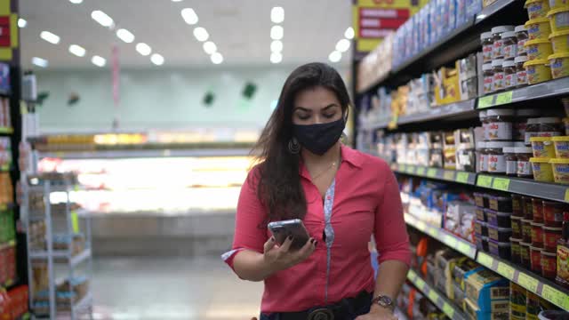 年轻女子戴着口罩在超市过道里检查商品视频素材