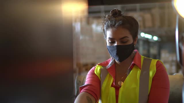 一名年轻女子在仓库里戴着面罩开着叉车的肖像视频下载